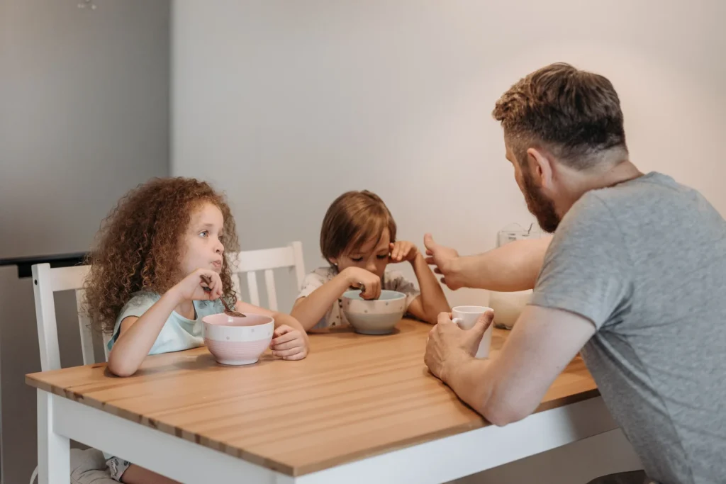 Adulto e crianças conversam durante o café da manhã à mesa.